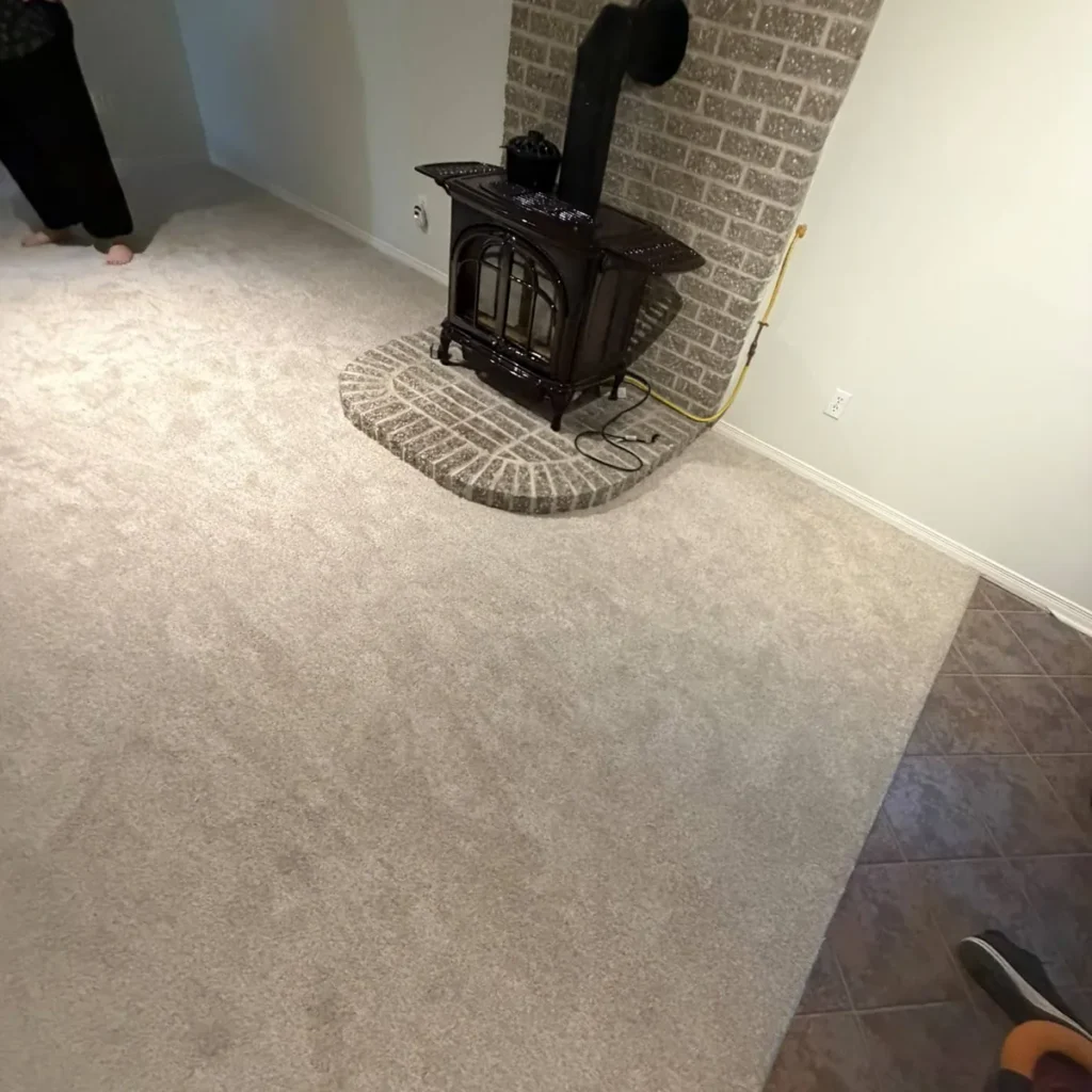 Grey plush carpet meeting a tile floor beside a brick hearth