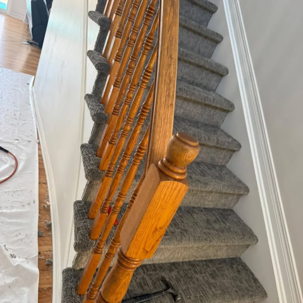 Grey textured stair carpet beside an oak railing and balusters